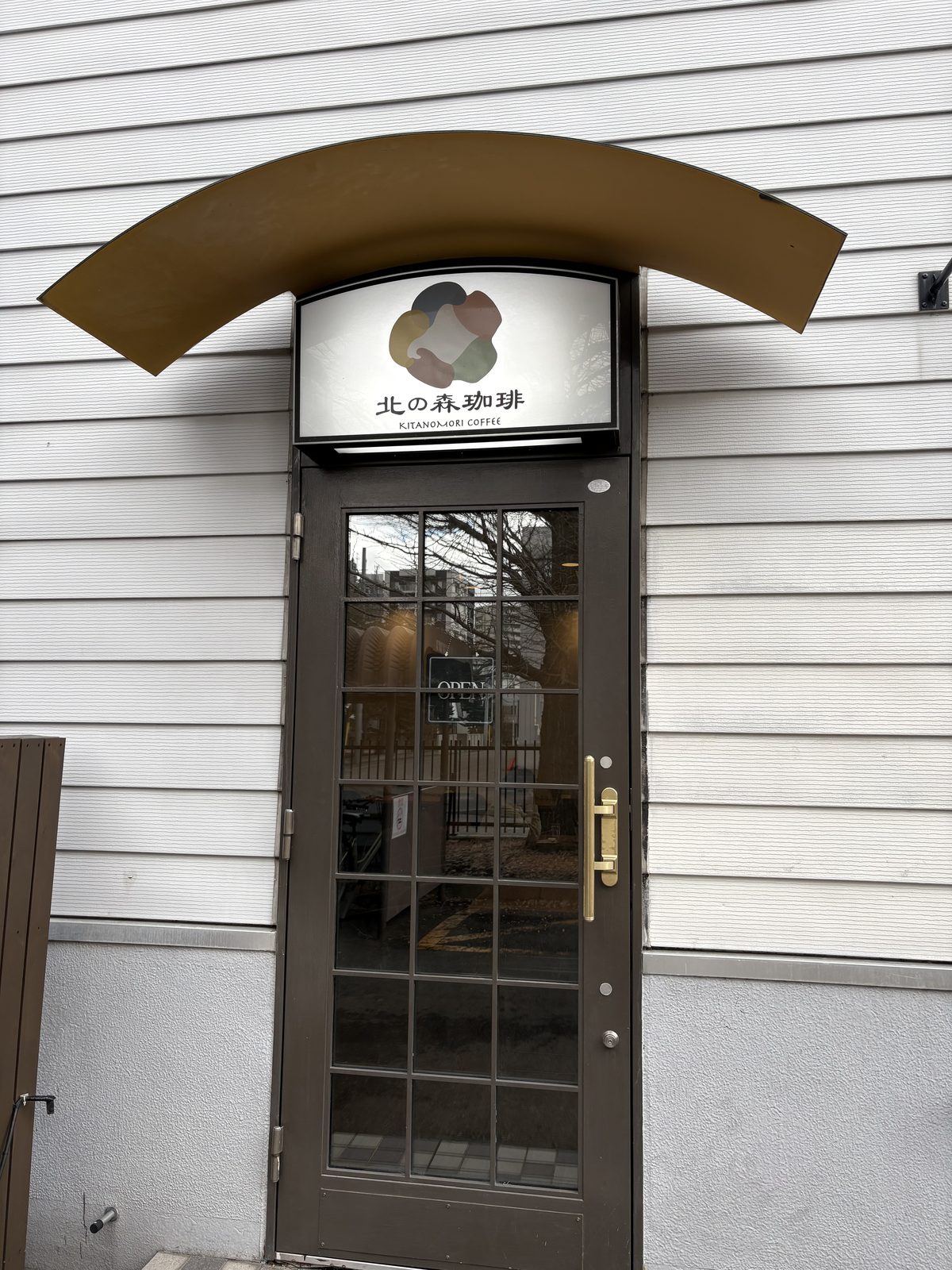 北の森珈琲の入口。アーチ屋根の下に北の森珈琲(KITANOMORI COFFEE)の看板とOPENの札