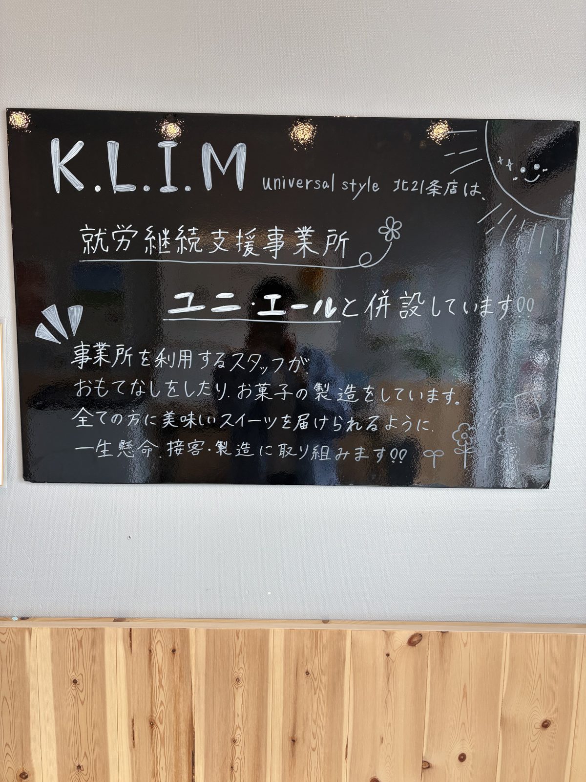 K.L.I.Mの店内にある「就労継続支援事業所ユニ・エールと併設しています」という説明の黒板
