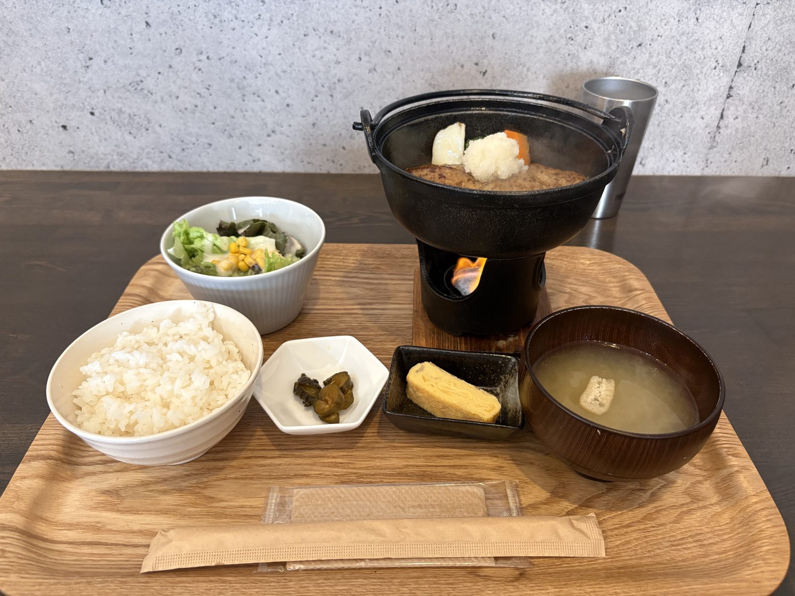 和風おろしハンバーグセット一式。ご飯・味噌汁・卵焼き・お漬物・サラダ・鉄鍋のハンバーグが並んでいる