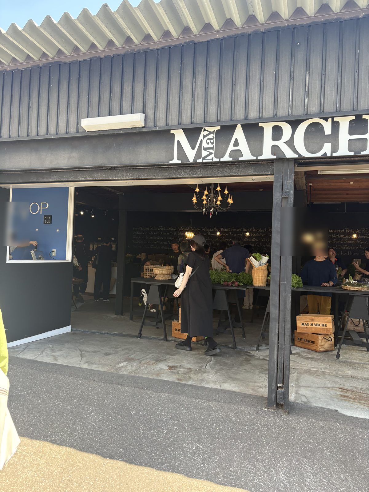 シャッターが開いたメイマルシェのガレージ。MARCHEのロゴとシャンデリア、野菜を選ぶ人たち
