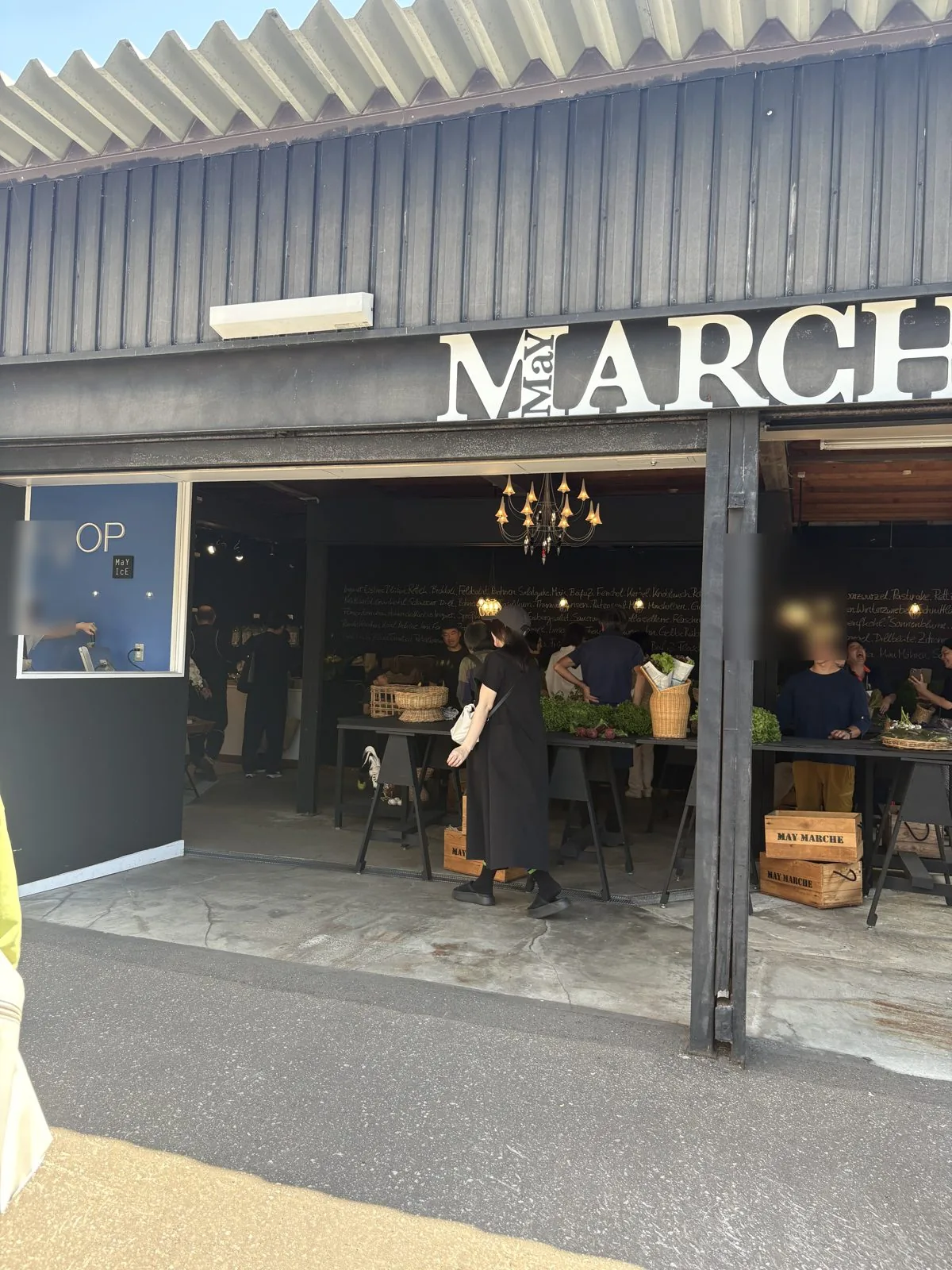 シャッターが開いたメイマルシェのガレージ。MARCHEのロゴとシャンデリア、野菜を選ぶ人たち