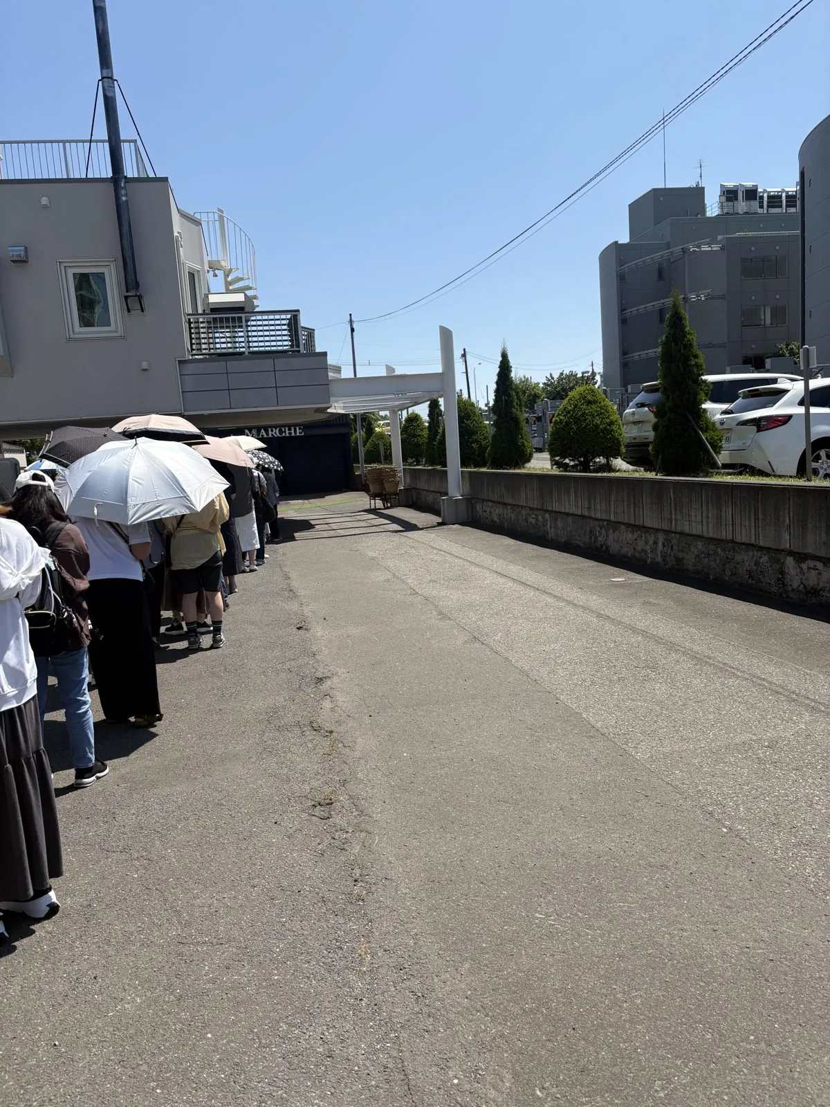 開店前のメイマルシェに並ぶ、日傘をさした人たちの行列