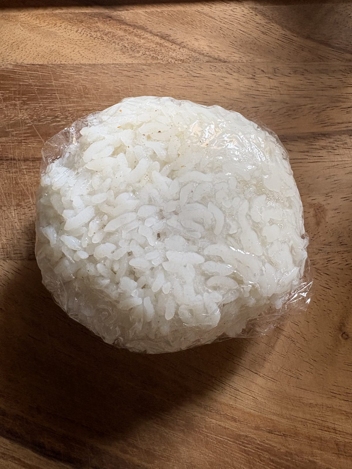 パックご飯で作ったおにぎり。ラップに包まれた丸いおにぎりが木のまな板の上にある