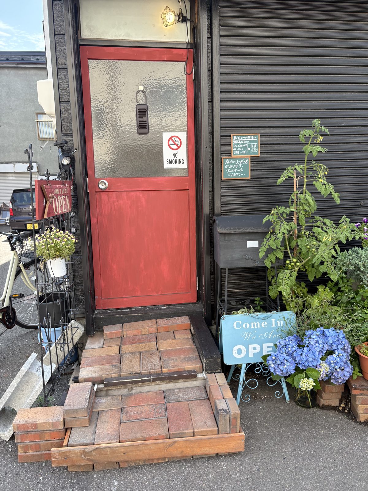 Bar Ziioの赤いドアの入口。レンガの階段とあじさいの鉢植え